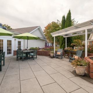 A spacious outdoor patio with furniture, green umbrellas, and a pergola adorned with plants.