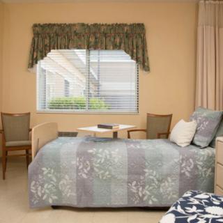 A cozy hospital room with a single bed, two chairs, and a window with curtains.
