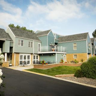 A modern residential building with blue siding and a landscaped yard under a clear sky.
