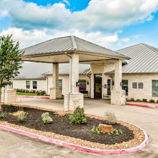 A modern entrance to a residential building, featuring landscaped surroundings and a cloudy sky.
