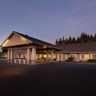An illuminated building exterior during the evening, surrounded by forested landscape.