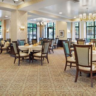 An elegant dining area with neatly arranged tables and chairs, featuring a carpeted floor and chandeliers overhead.