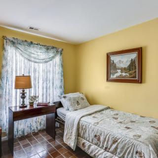A cozy bedroom with a single bed, decorated with yellow walls, a window with curtains, and a lamp on a bedside table.