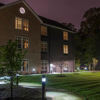 A well-lit building at night with a grassy area and pathway.