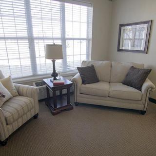 A cozy living room with a sofa, armchair, and a lamp by the window.