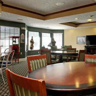 A cozy dining area with a large round table, several chairs, and a television in the background.