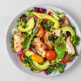 A colorful and fresh chicken salad with avocado, mixed greens, and pomegranate seeds.