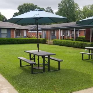 A peaceful courtyard with picnic tables and umbrellas on a well-maintained lawn surrounded by buildings.
