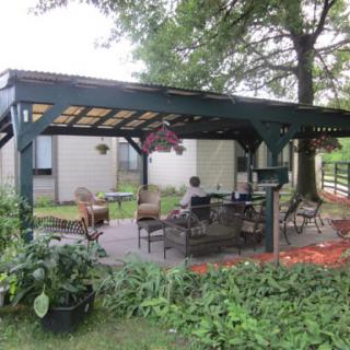A serene outdoor patio area shaded by a canopy, surrounded by greenery.