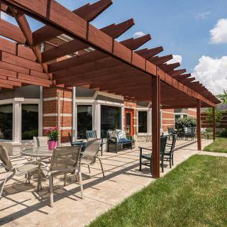 A backyard patio featuring a wooden pergola over outdoor seating and a table, adjacent to a brick house.