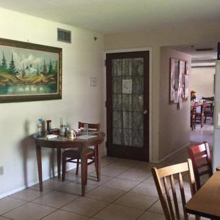 A cozy restaurant interior featuring a small dining area with wooden tables and chairs, decorated with a painting on the wall.