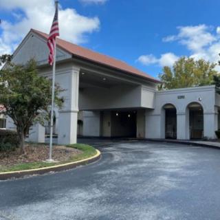 A view of a building entrance with an American flag, surrounded by trees and under a partly cloudy sky.
