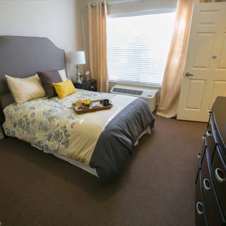 A cozy and well-decorated bedroom with a neatly made bed, pillows, and a tray, complemented by natural light streaming through the window.
