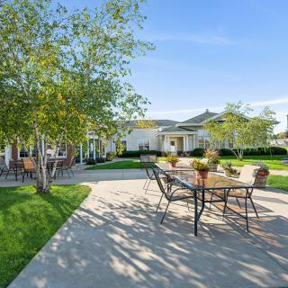 A sunny patio area with tables and chairs surrounded by a landscaped garden.