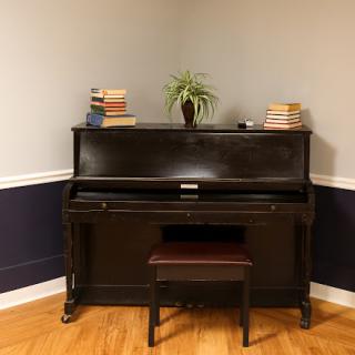 A classic black piano with a cozy setup, adorned with books and a small plant.