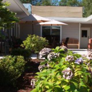 A well-maintained garden with blooming flowers next to a patio area in front of a house.