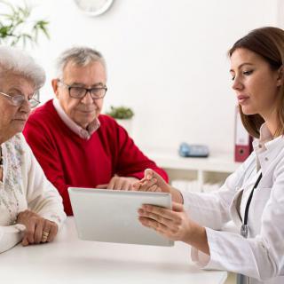 A doctor is consulting an elderly couple using a tablet during a healthcare appointment.