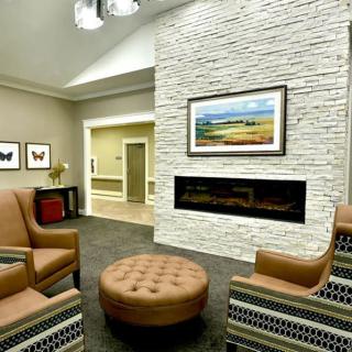 A modern living room with a cozy seating area around a sleek fireplace, featuring artwork and stylish decor.