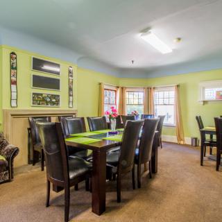 A spacious dining room with a large table and multiple chairs, featuring bright walls and ample natural light from the windows.