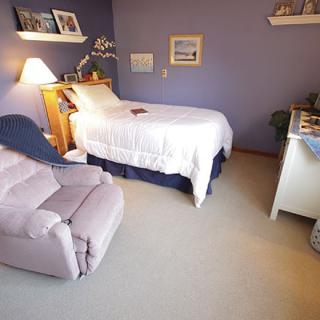 A cozy bedroom with a bed, recliner, and soft lighting.