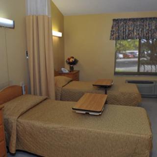 A hospital room with two beds, a privacy curtain, and a window.