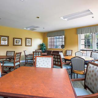 A well-lit communal dining room with several tables and chairs, decorated with framed pictures on the walls.