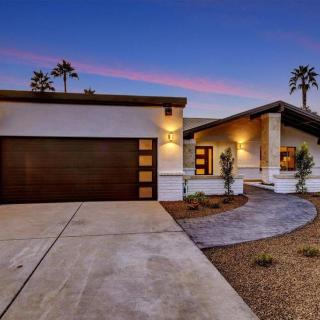 A modern house with a garage and exterior lighting at dusk, surrounded by palm trees.