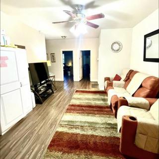 A cozy living room with a sofa, large television, rug, and ceiling fan.