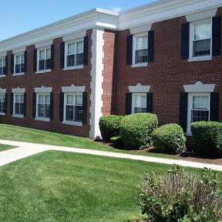 A brick building with multiple windows, surrounded by well-maintained landscaping and a sidewalk.
