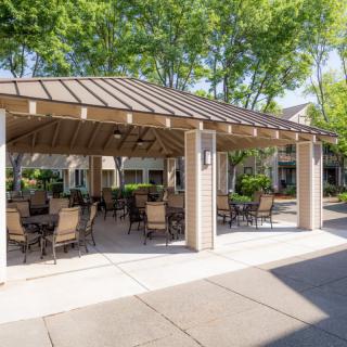 A spacious outdoor seating area under a wooden gazebo in a lush garden setting.