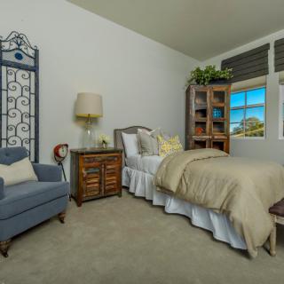 A cozy bedroom featuring a bed with neutral bedding, a blue armchair, and a wooden nightstand under a lamp.