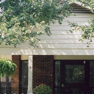 A brick and siding residential house with a front yard and trees.