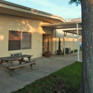 A small building with a patio area, featuring a picnic table and green grass in the foreground, illuminated by the setting sun.
