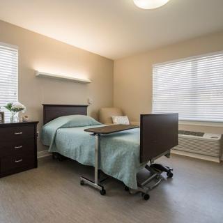 A clean and well-lit hospital room with a single bed and bedside furniture.
