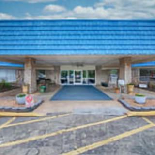 The front entrance of a building with a blue roof and adjacent parking lot.