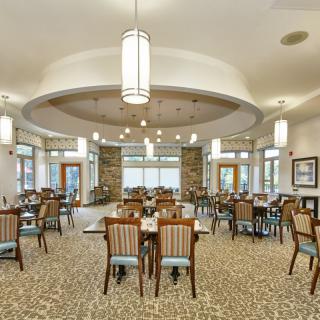 A spacious dining area with neatly arranged tables and chairs, featuring elegant lighting fixtures and large windows.