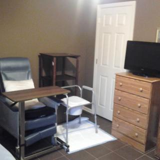 A small room featuring a comfortable chair with a table, a dresser with a television on top, and shelves in the corner.