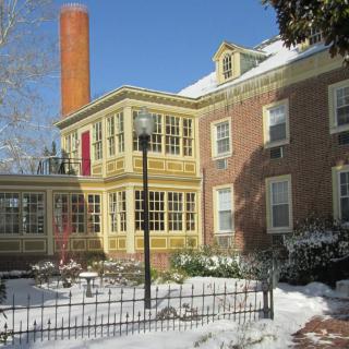 A brick house with large windows and a tall chimney, surrounded by snow on a clear winter day.