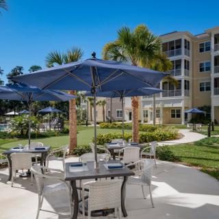 A sunny outdoor patio at a resort, featuring tables with umbrellas and surrounded by lush landscaping.