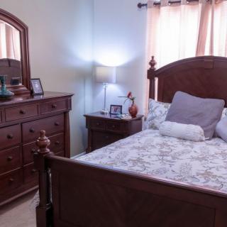 A cozy bedroom with a wooden bed and dresser, softly lit by a bedside lamp.