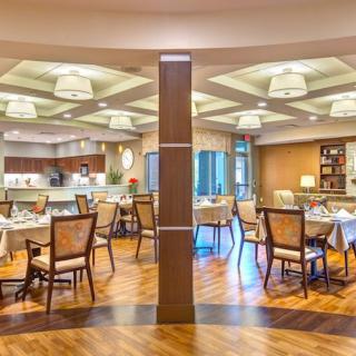 A modern restaurant interior with neatly arranged tables and chairs, elegant lighting, and a warm wooden floor.