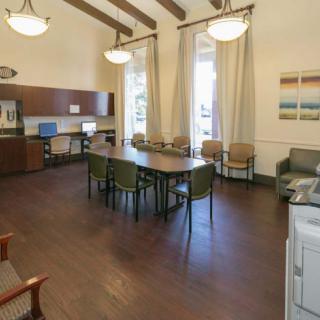 A spacious meeting room with a large table, chairs, and computer stations, featuring high ceilings and wooden flooring.