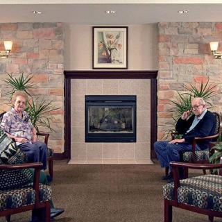 Two elderly individuals relaxing in a cozy living room with a fireplace.