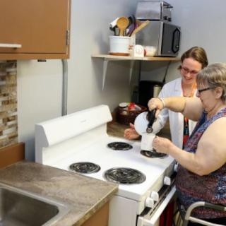 Two people working together in a kitchen, using the stove.