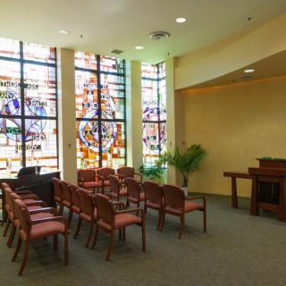 A small chapel with stained glass windows and rows of chairs.