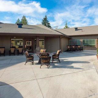 A spacious outdoor patio area with furniture, set against a house and surrounded by greenery under a clear blue sky.