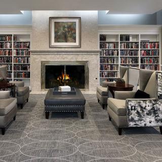 A cozy library setting with a fireplace, surrounded by bookshelves and comfortable armchairs.
