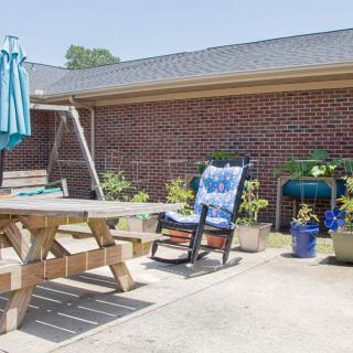 A sunny patio with a picnic table, rocking chair, and potted plants.