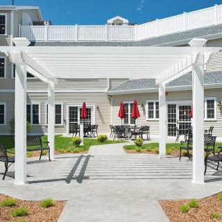 A scenic outdoor patio area with a pergola, surrounded by tables and chairs in front of a building.