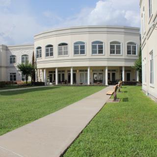 A modern educational building with a circular design and wide windows, surrounded by a grassy area and a paved walkway.
